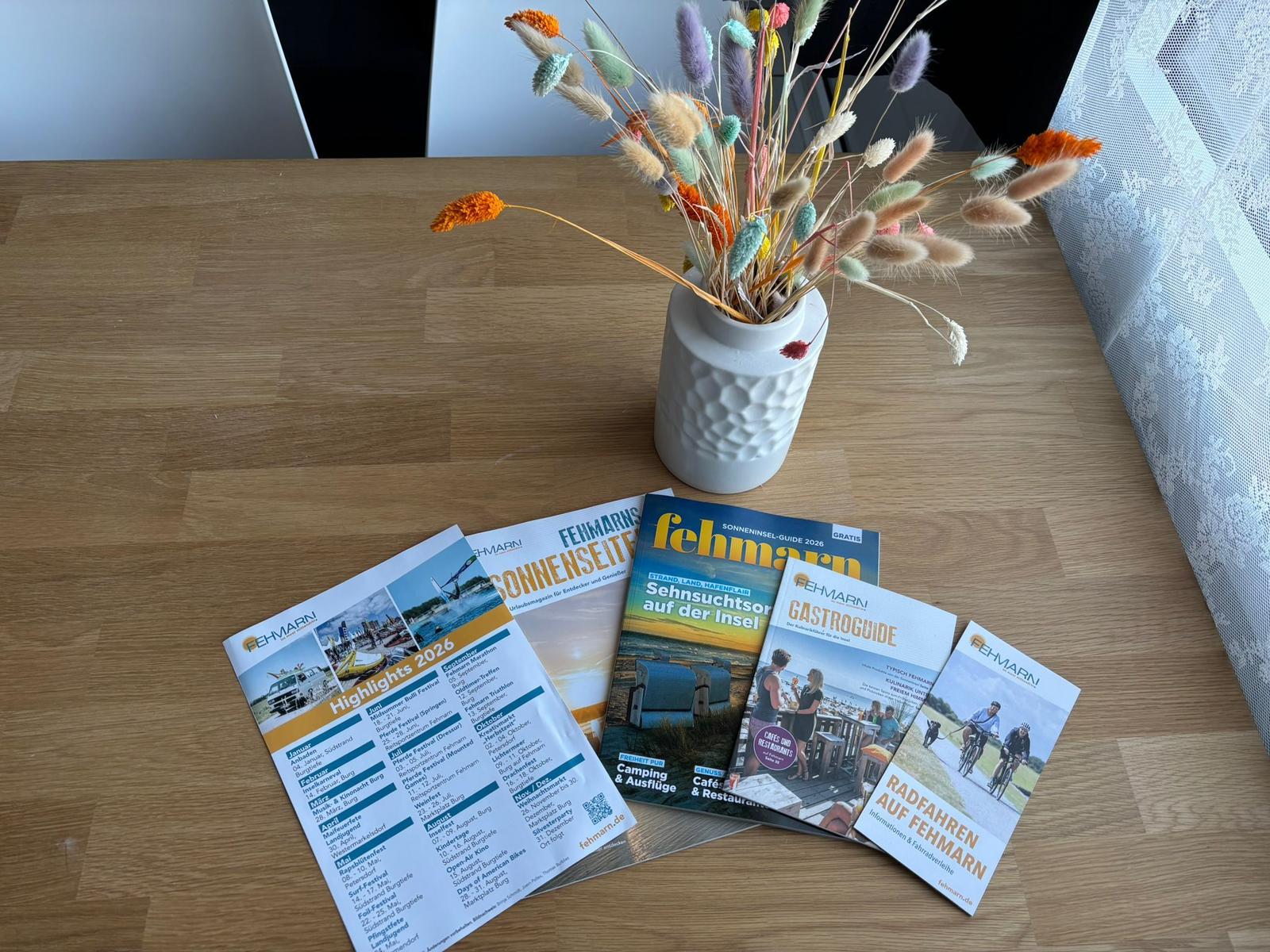 Holztisch mit Blumen und Fehmarn-Reiseführern.