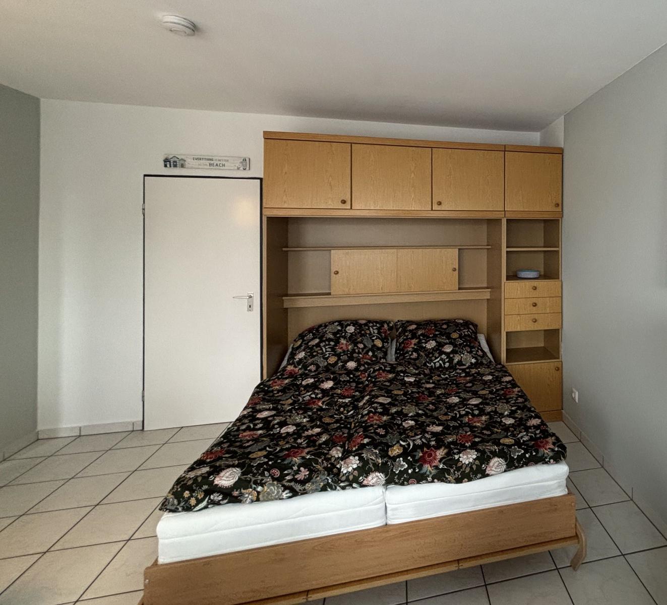 Schlafzimmer mit Bett und Holzmöbeln, Tür und Fliesenboden