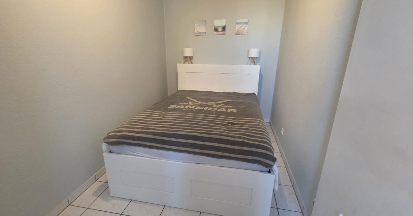 Schlafzimmer mit weißem Bett und gestreifter Bettdecke.