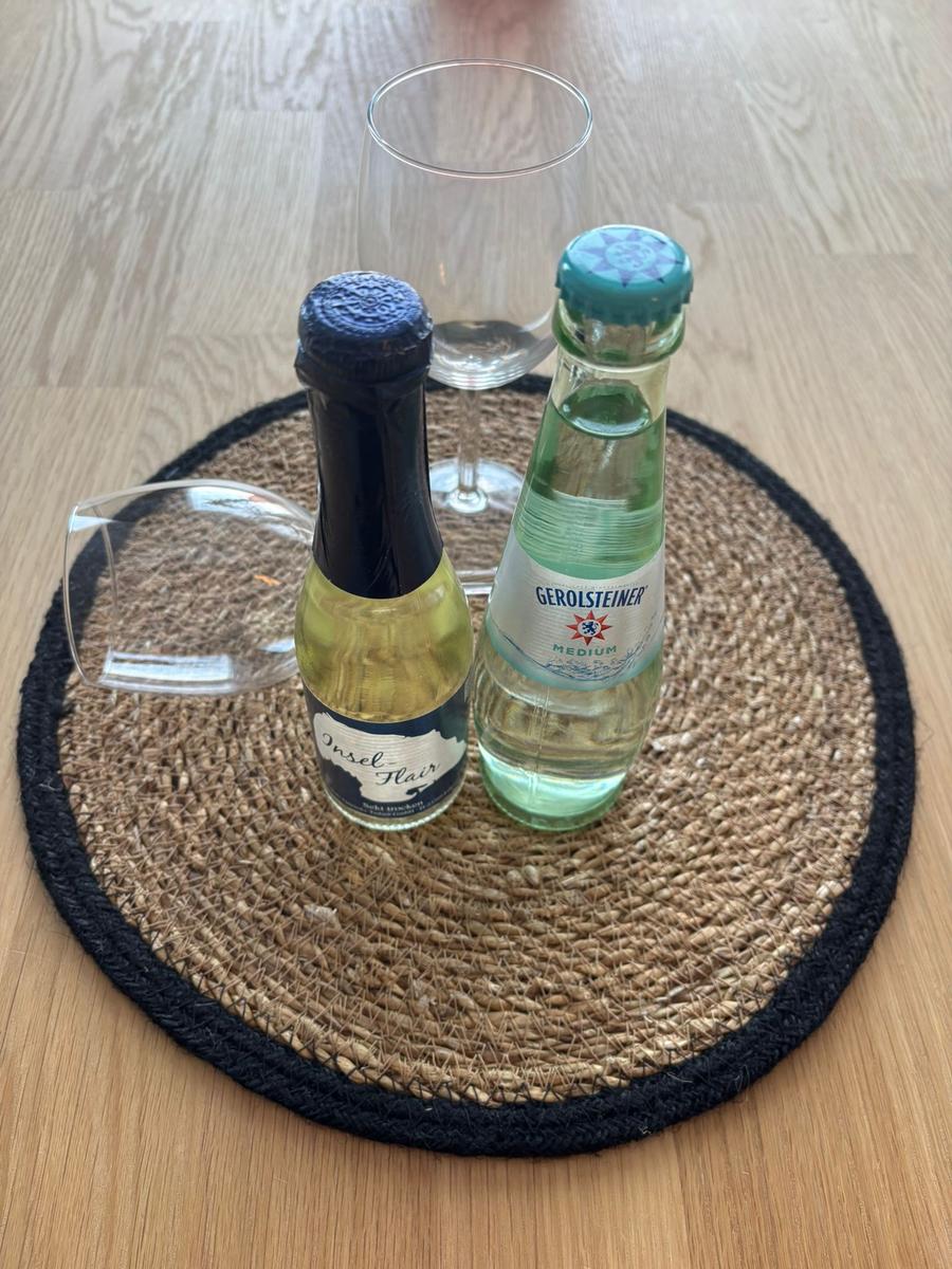 Zwei Getränkeflaschen und ein Weinglas auf einem runden Tischset.