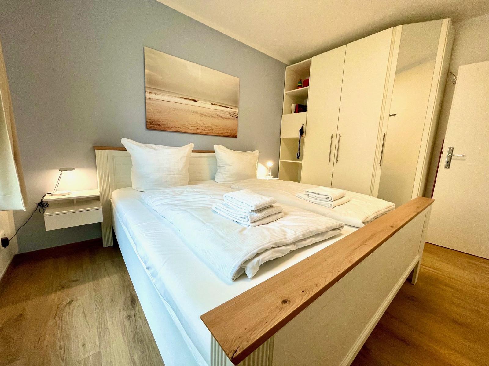 Schlafzimmer mit Doppelbett, Kleiderschrank und Wandbild.