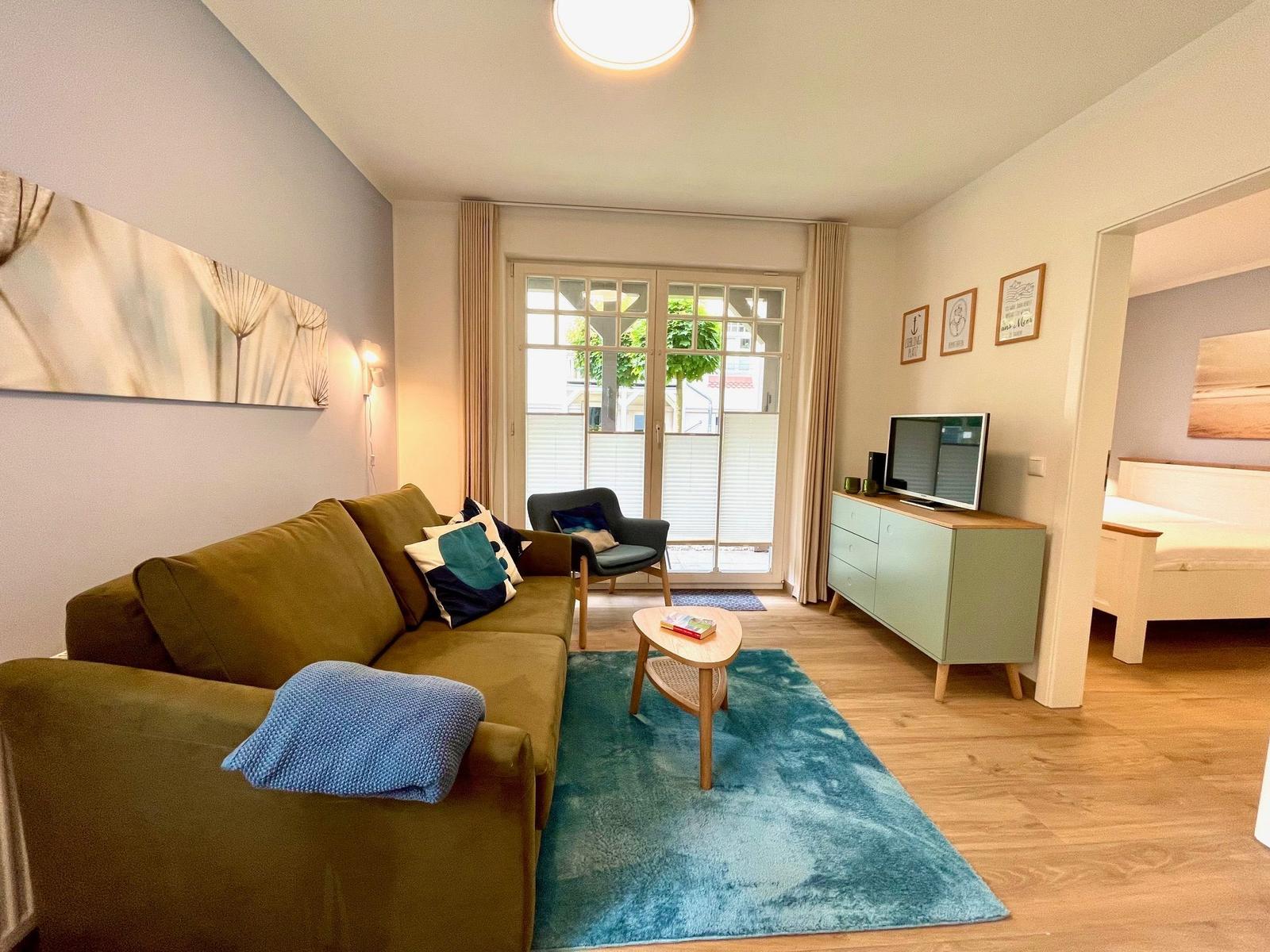 Wohnzimmer mit Sofa, Couchtisch und Fernseher. Durchgang zur Schlafzimmer.