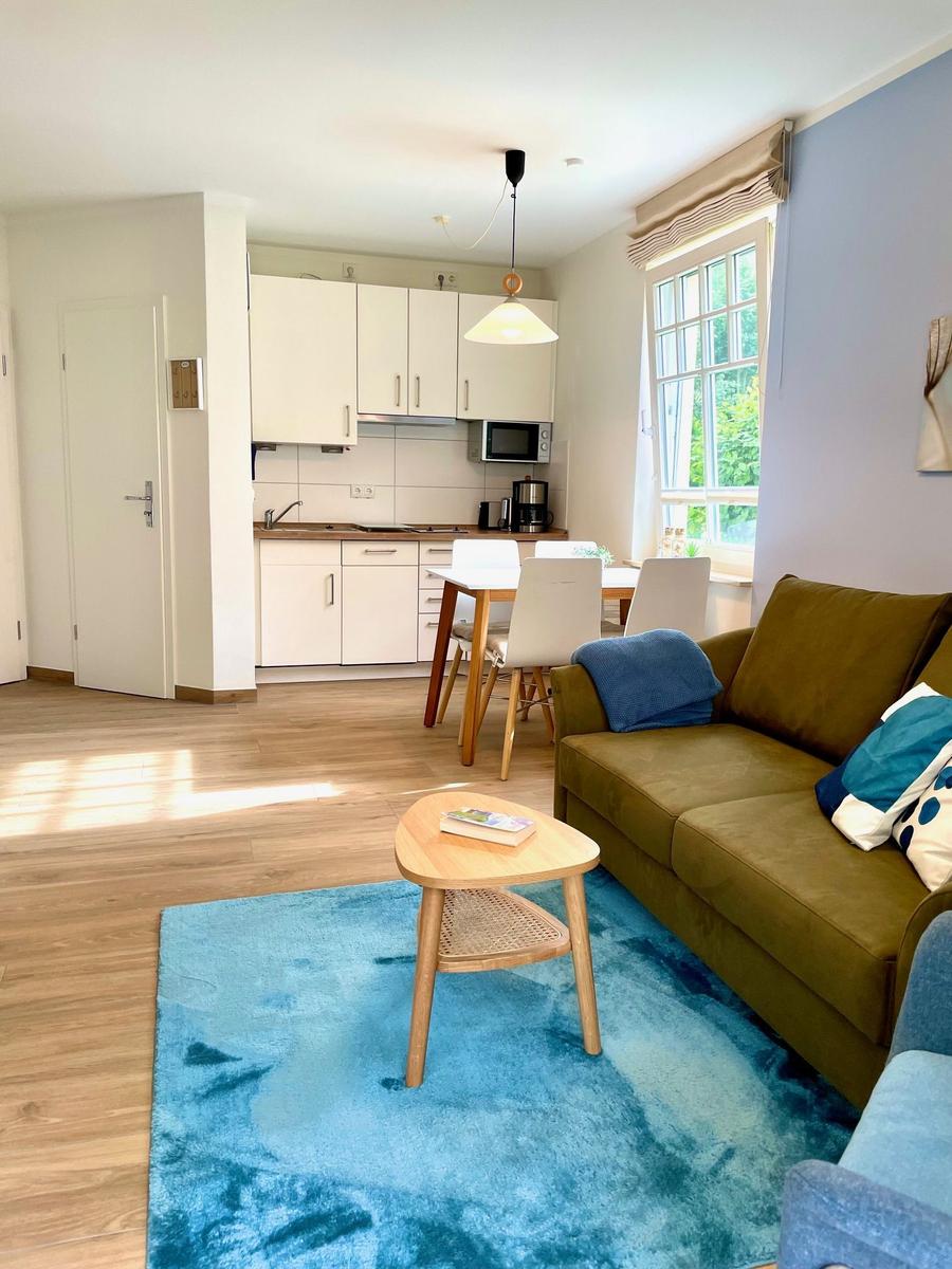 Wohnzimmer mit Sofa, Tisch und Küche im Hintergrund.