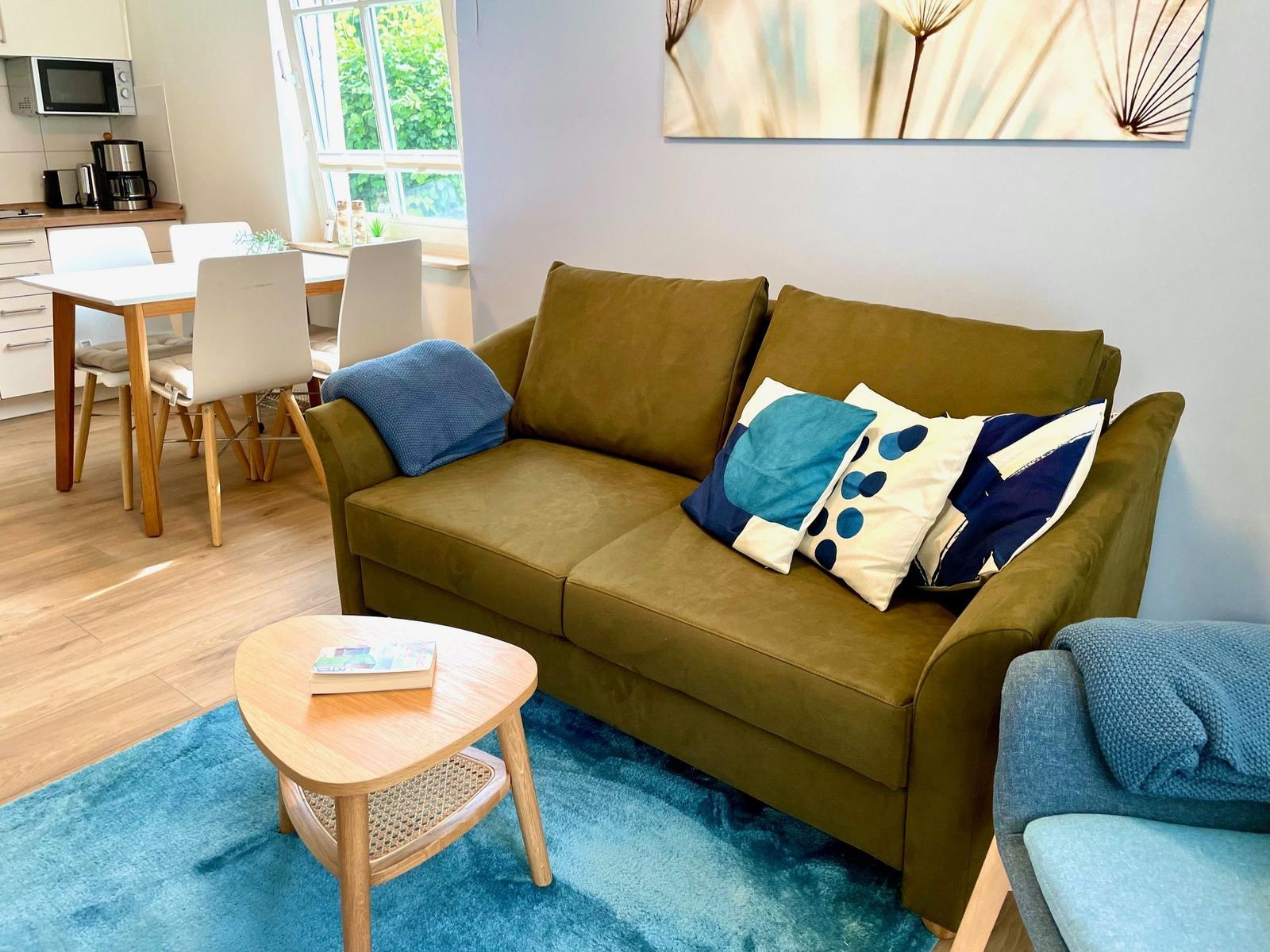 Ein Wohnzimmer mit Sofa, Tisch und Blauem Teppich.