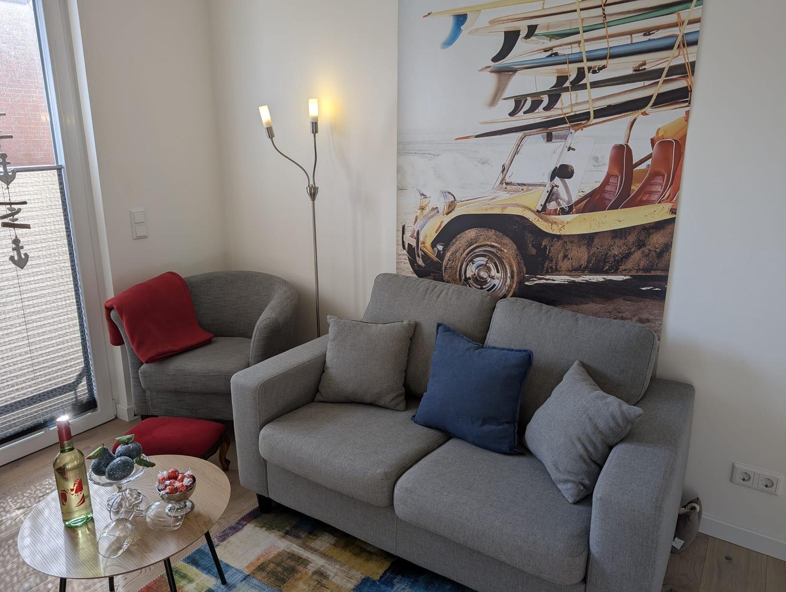 Wohnzimmer mit grauem Sofa, Kissen und Wandbild mit Oldtimer. 