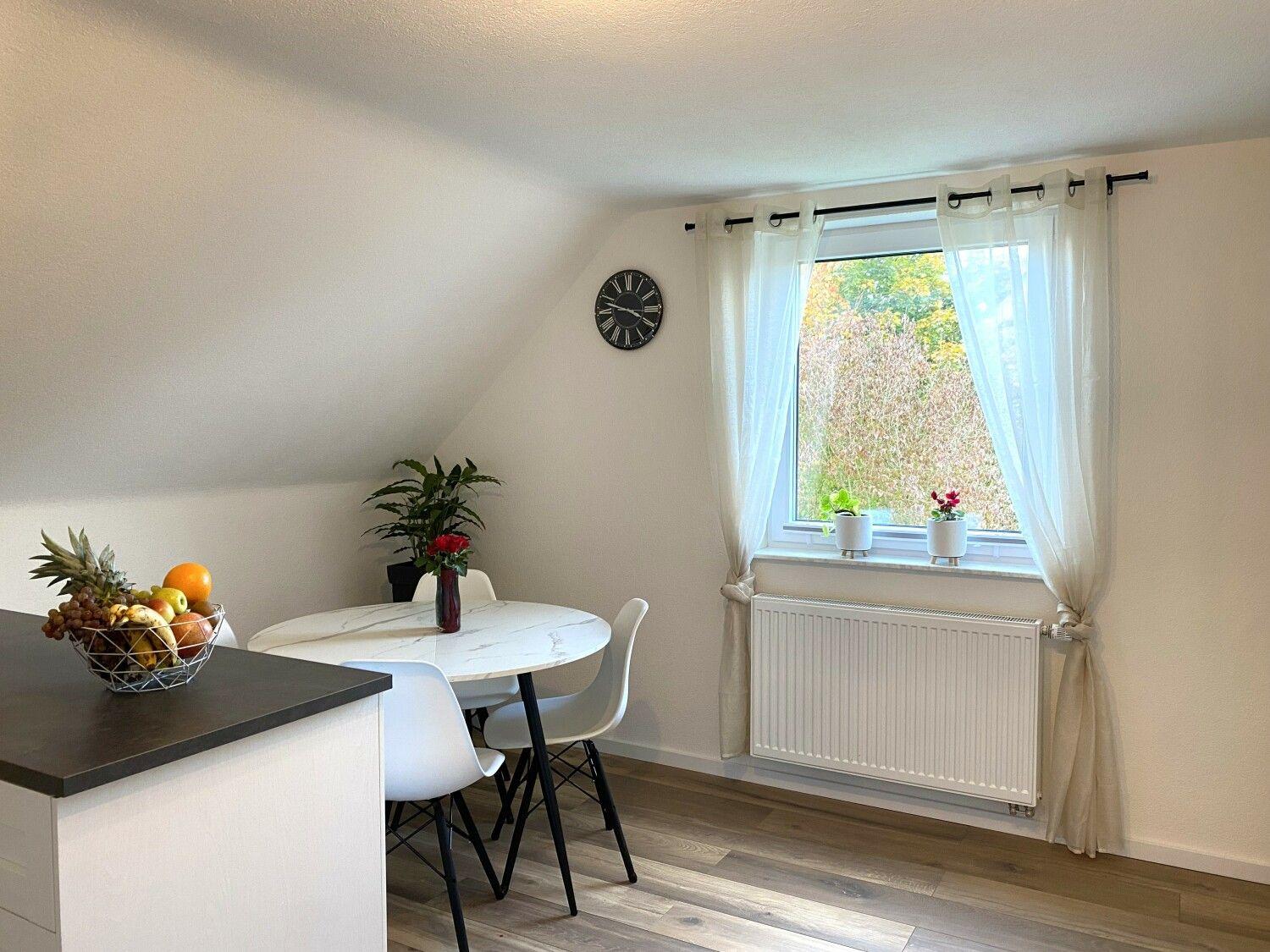 Essbereich mit runden Tisch, weißen Stühlen und Fenster mit weißen Vorhängen.