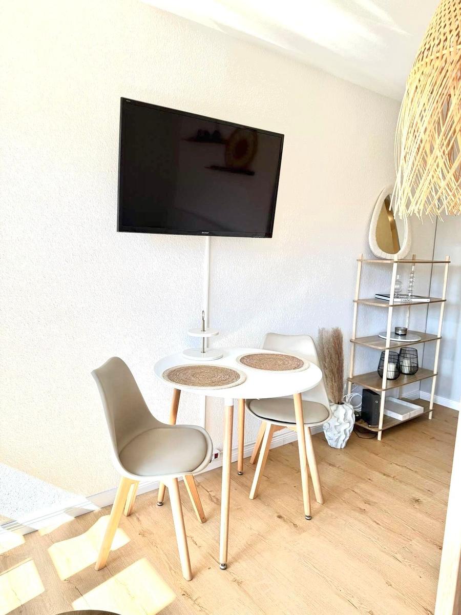 Runde Esstisch mit Stühlen, Wandfernseher und Regal im Raum.