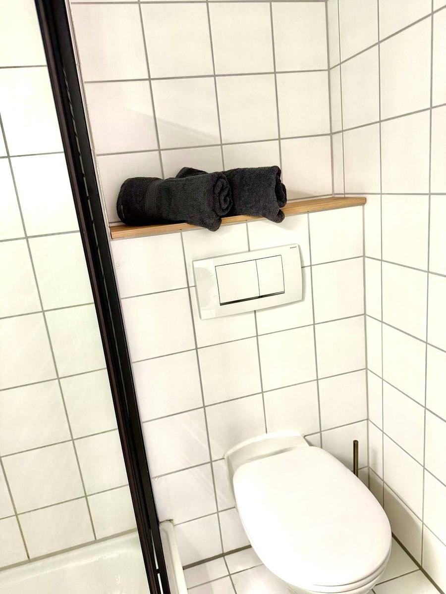 Badezimmer mit Toilette, Dusche und schwarzen Handtüchern auf Holzregal.