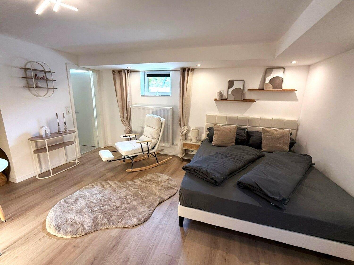 Schlafzimmer mit Doppelbett, Sessel und Fenster.