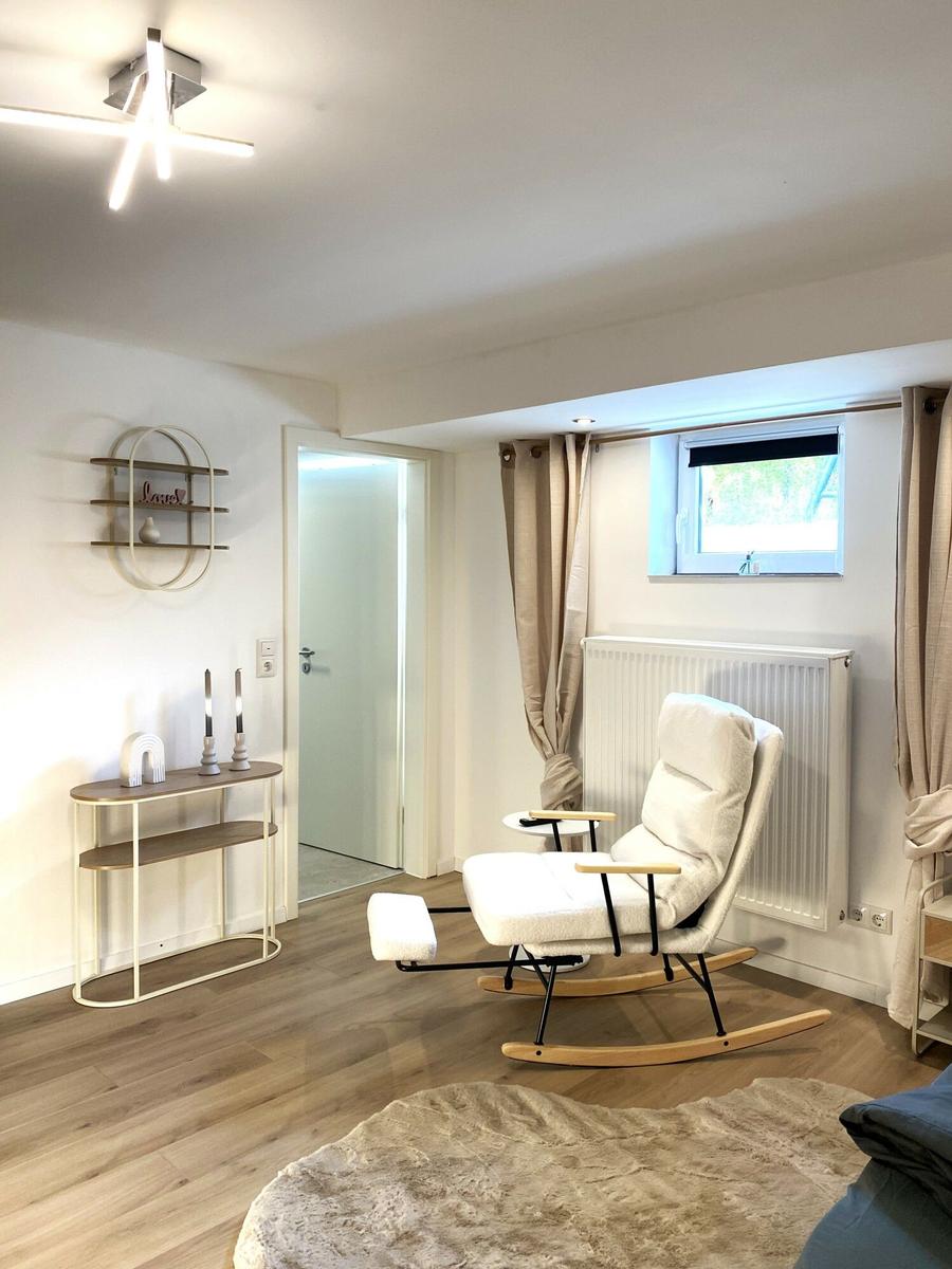 Ein Raum mit weißem Schaukelstuhl, Holzboden und Fenster mit Vorhängen.