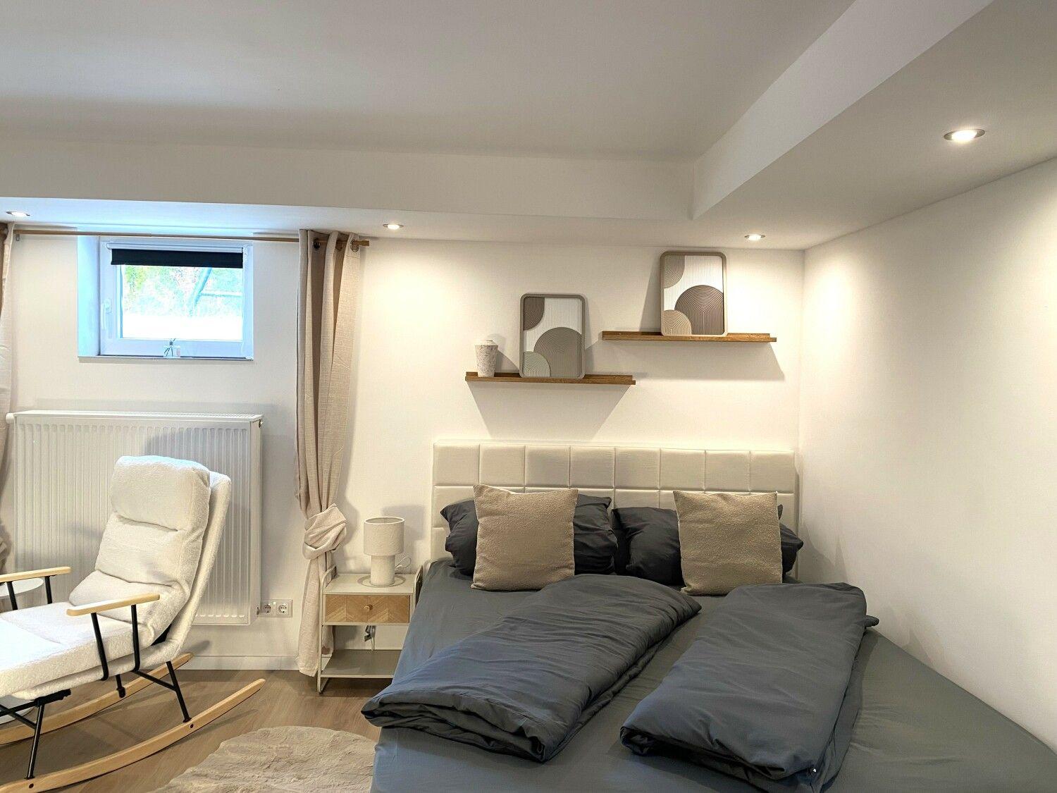 Schlafzimmer mit Doppelbett, Schaukelstuhl und Fenster.