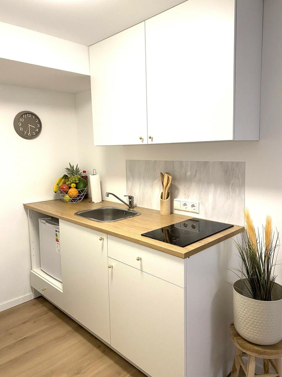 Küche mit weißen Schränken, Holzplatte, Spüle und Induktionskochfeld.
