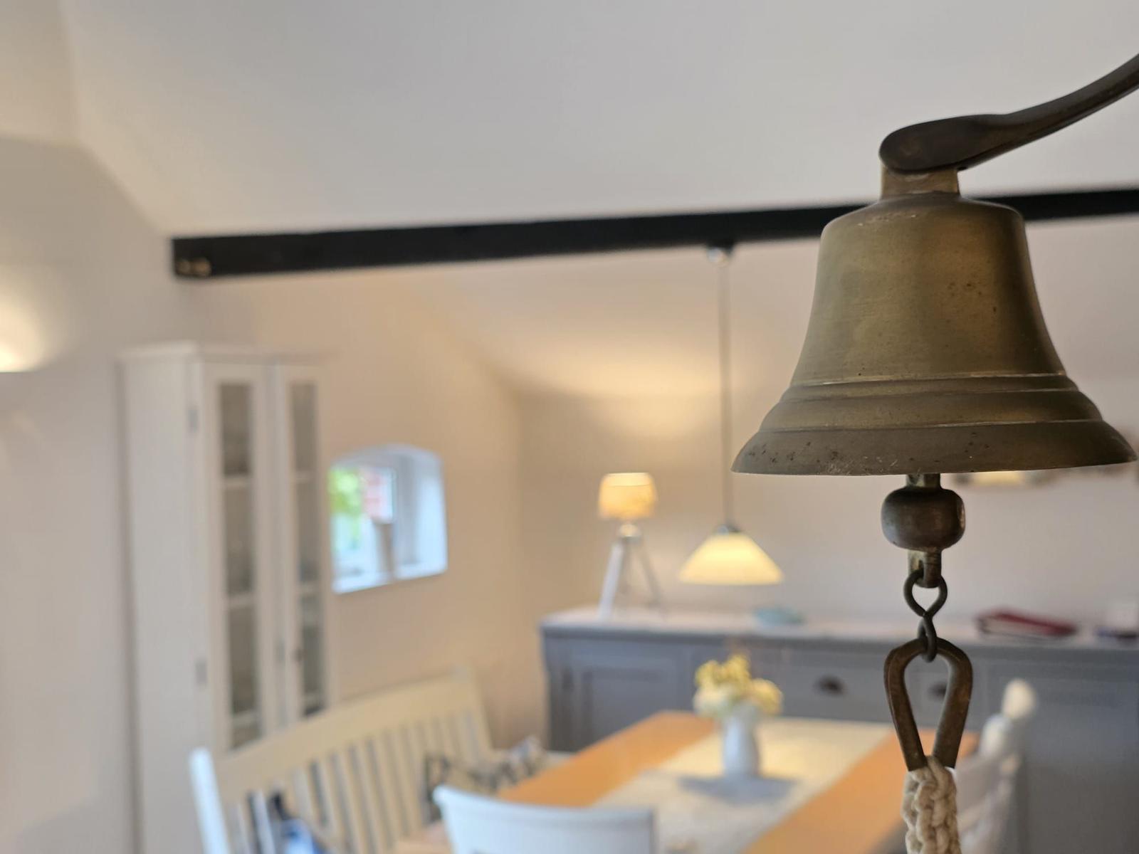 Vintage bell in foreground, dining room with table and chairs in background.