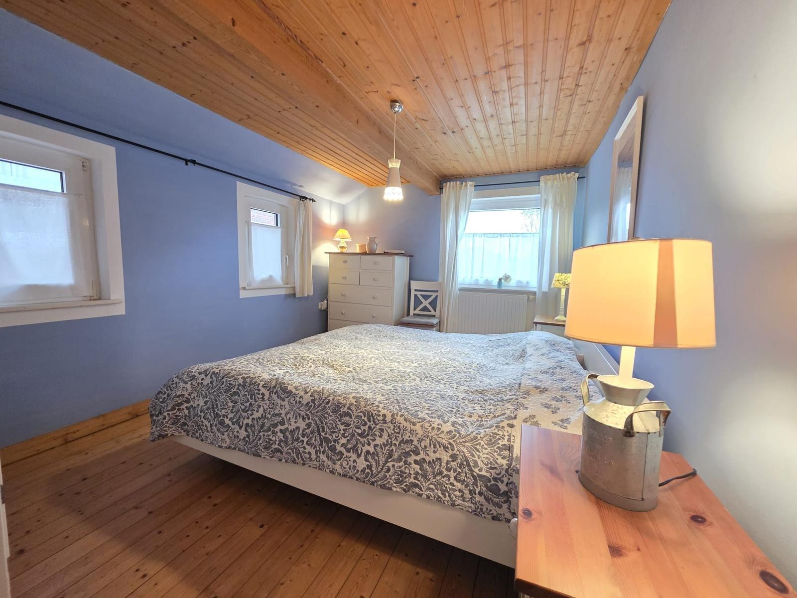 Bedroom with wooden floor, blue walls, and wooden ceiling. Bed, nightstand, and dresser are present.