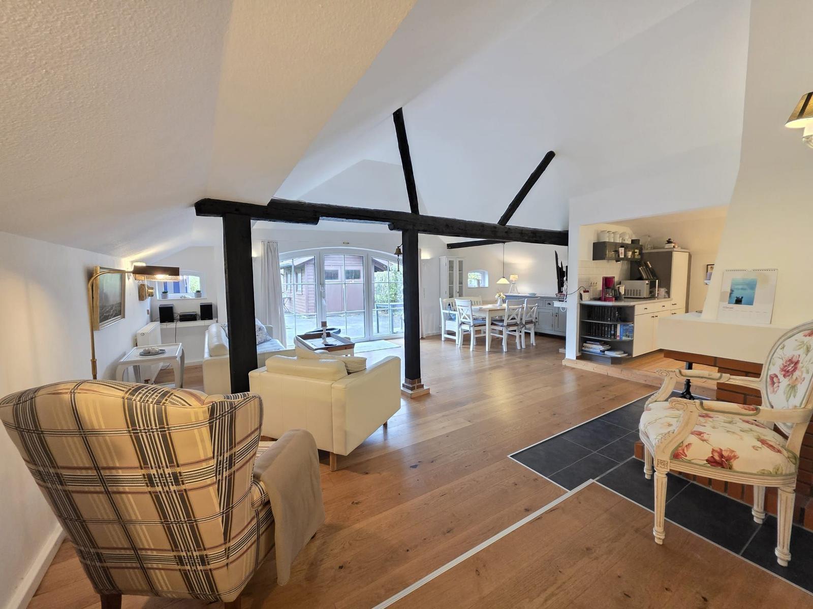 Living and dining area with wooden floor and black beams. Furniture including chairs and sofa.