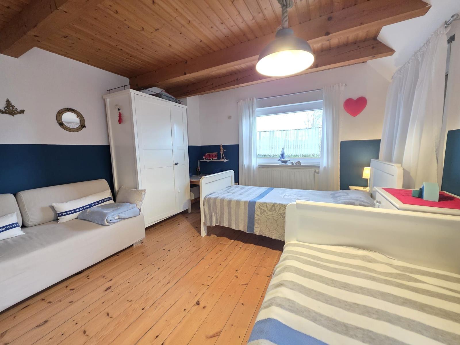 Room with two beds, sofa, wardrobe, and wooden floor.