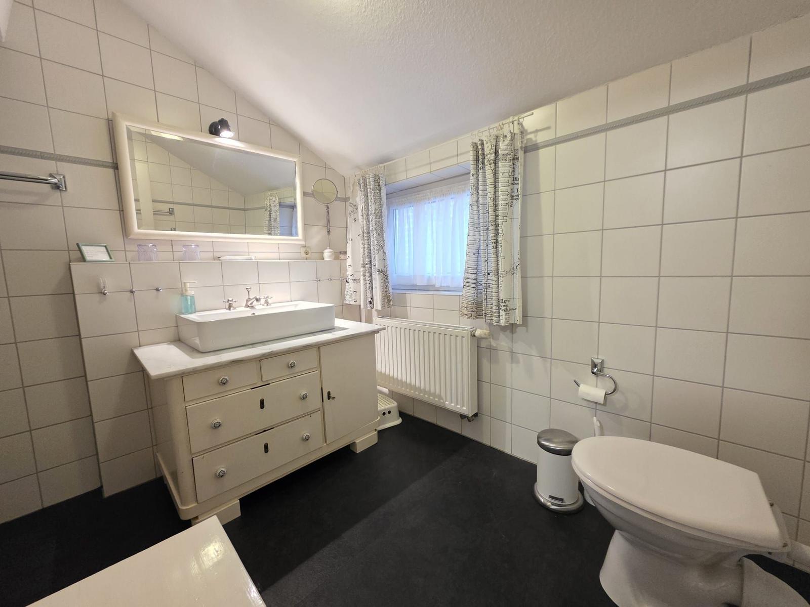 Bathroom with sink, mirror, toilet, and window.
