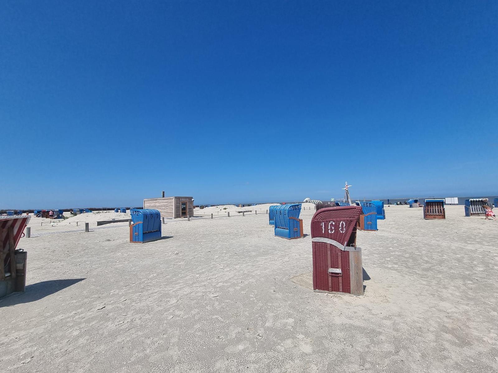 Beach with beach chairs and small wooden house under blue sky.