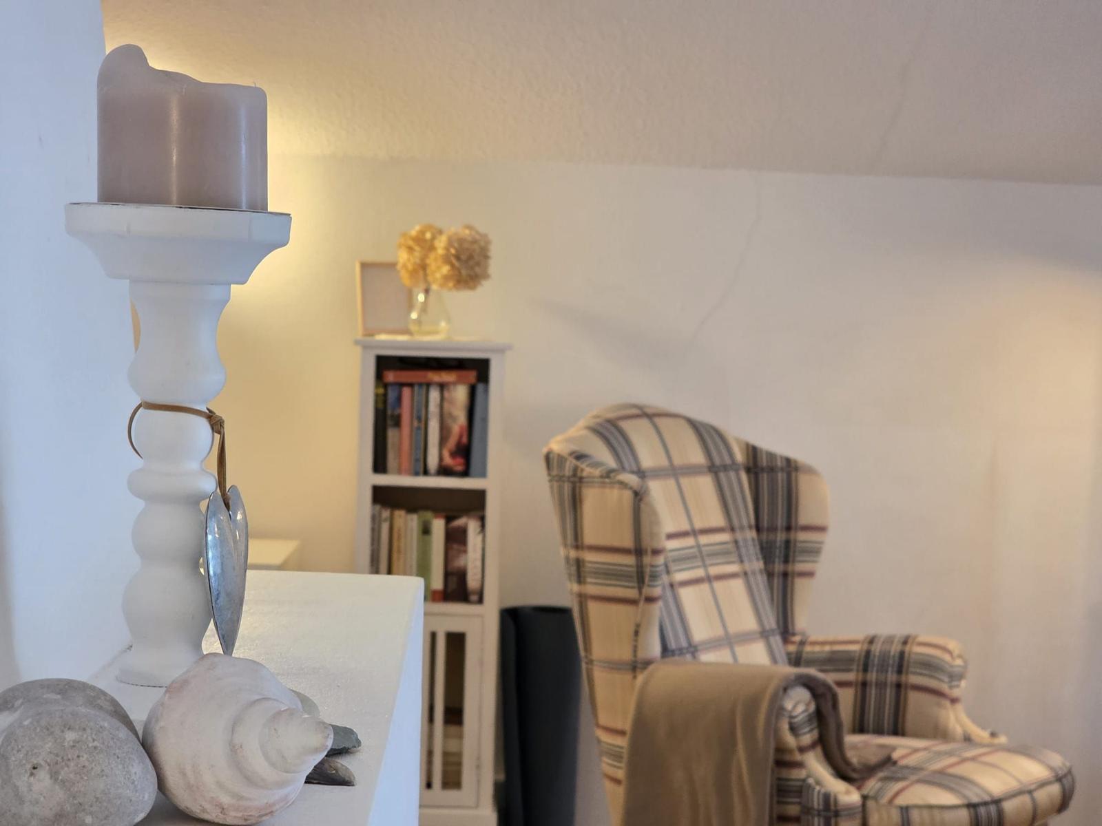 Room with armchair, bookshelf, and candle holder with seashells.