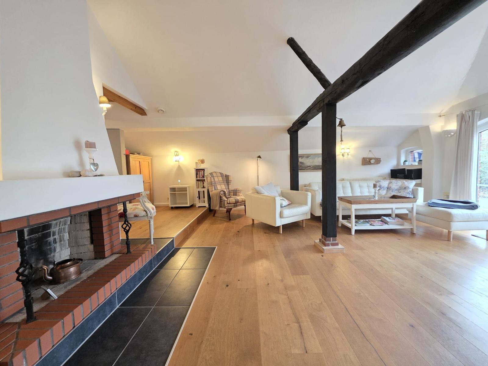Living room with fireplace, wooden floor, and heavy beams. Furniture is light and modern.