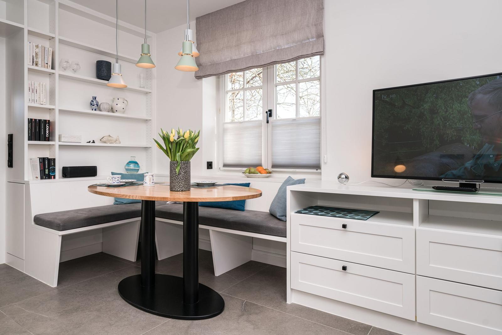 Essbereich mit Sitzbank, Tisch und Fernseher an der Wand.