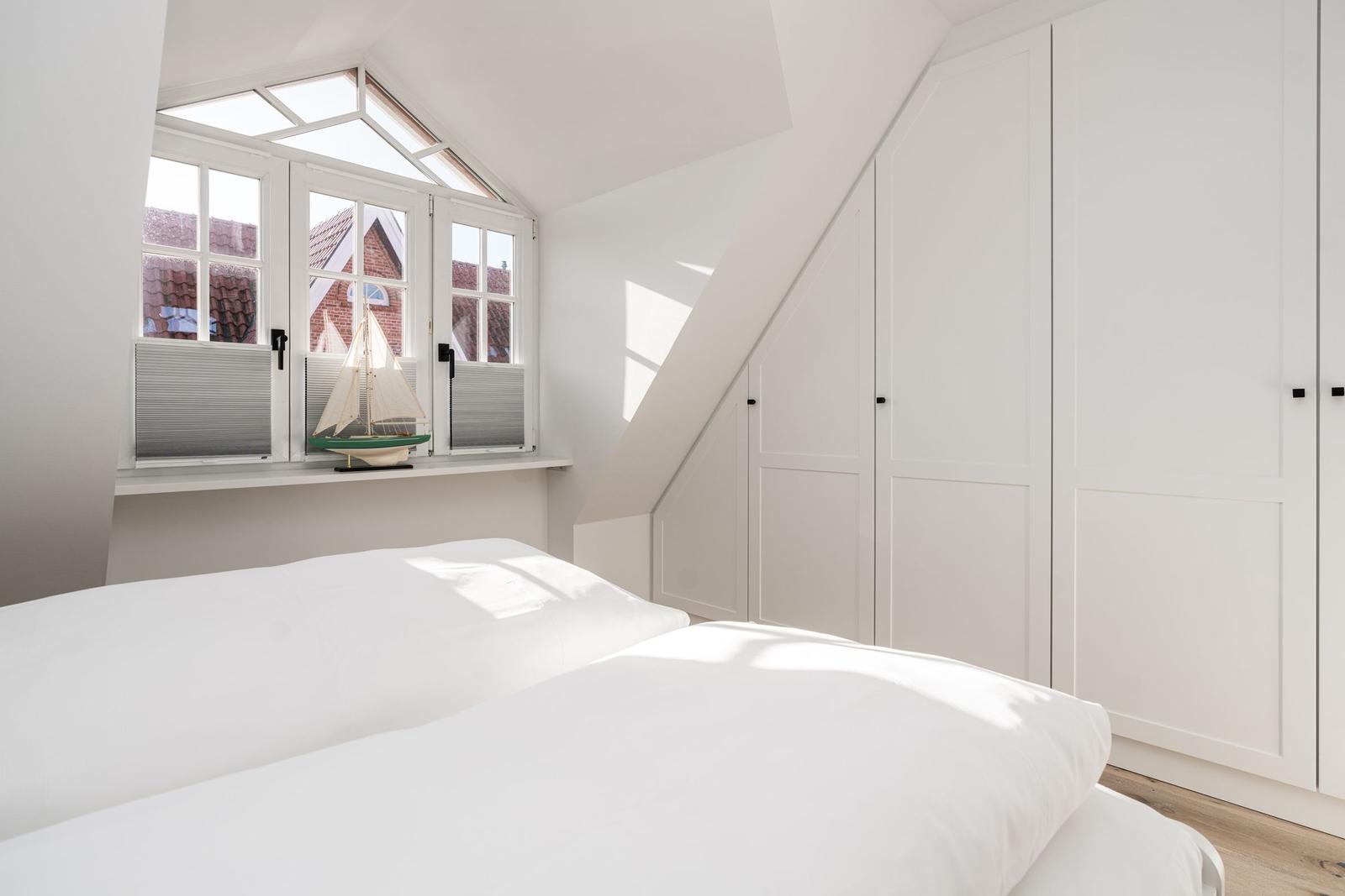 Schlafzimmer mit weißem Bett, Fenster und Kleiderschrank.