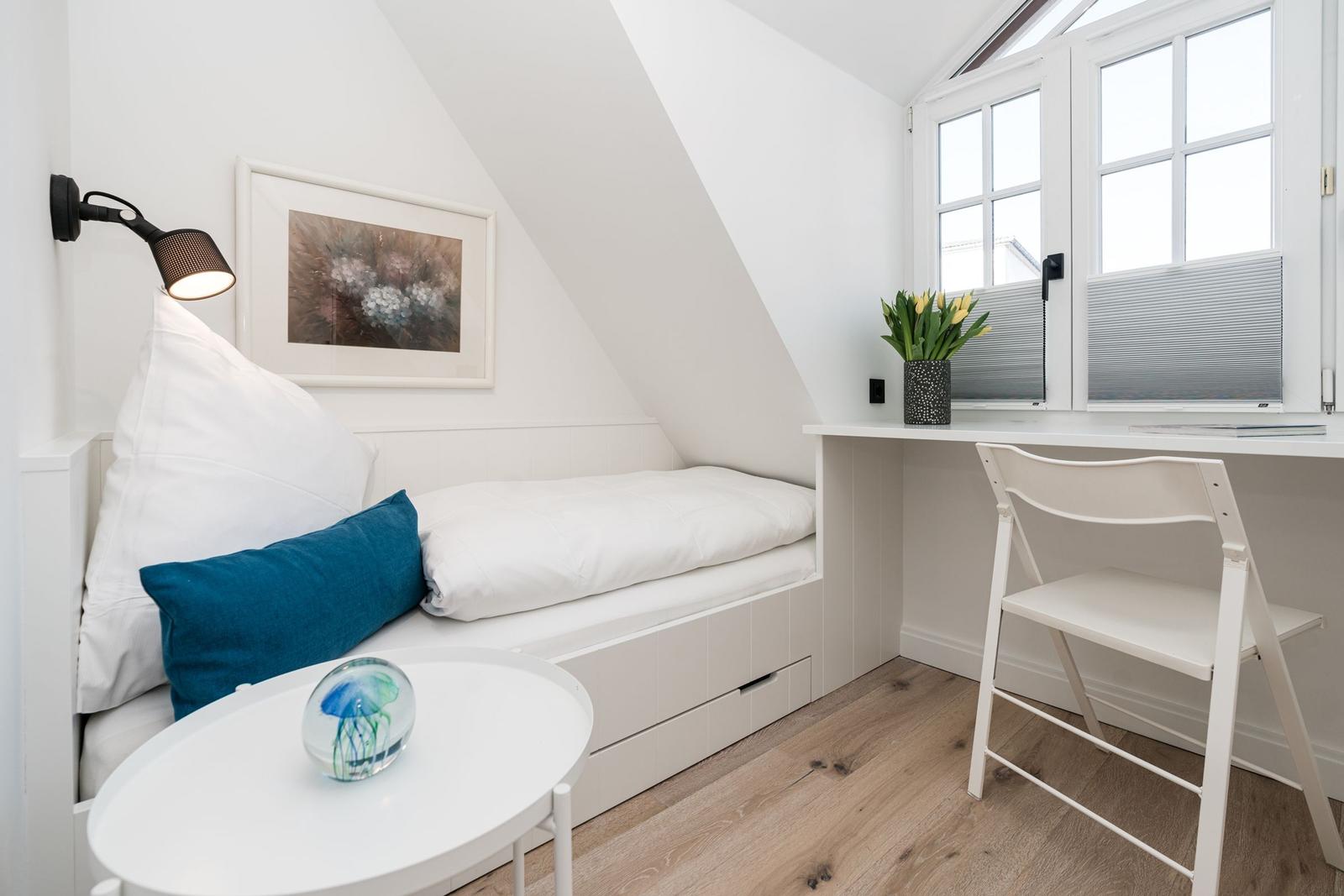 Schlafzimmer mit Bett, Schreibtisch und Fenster. Holzboden und weiße Wände.