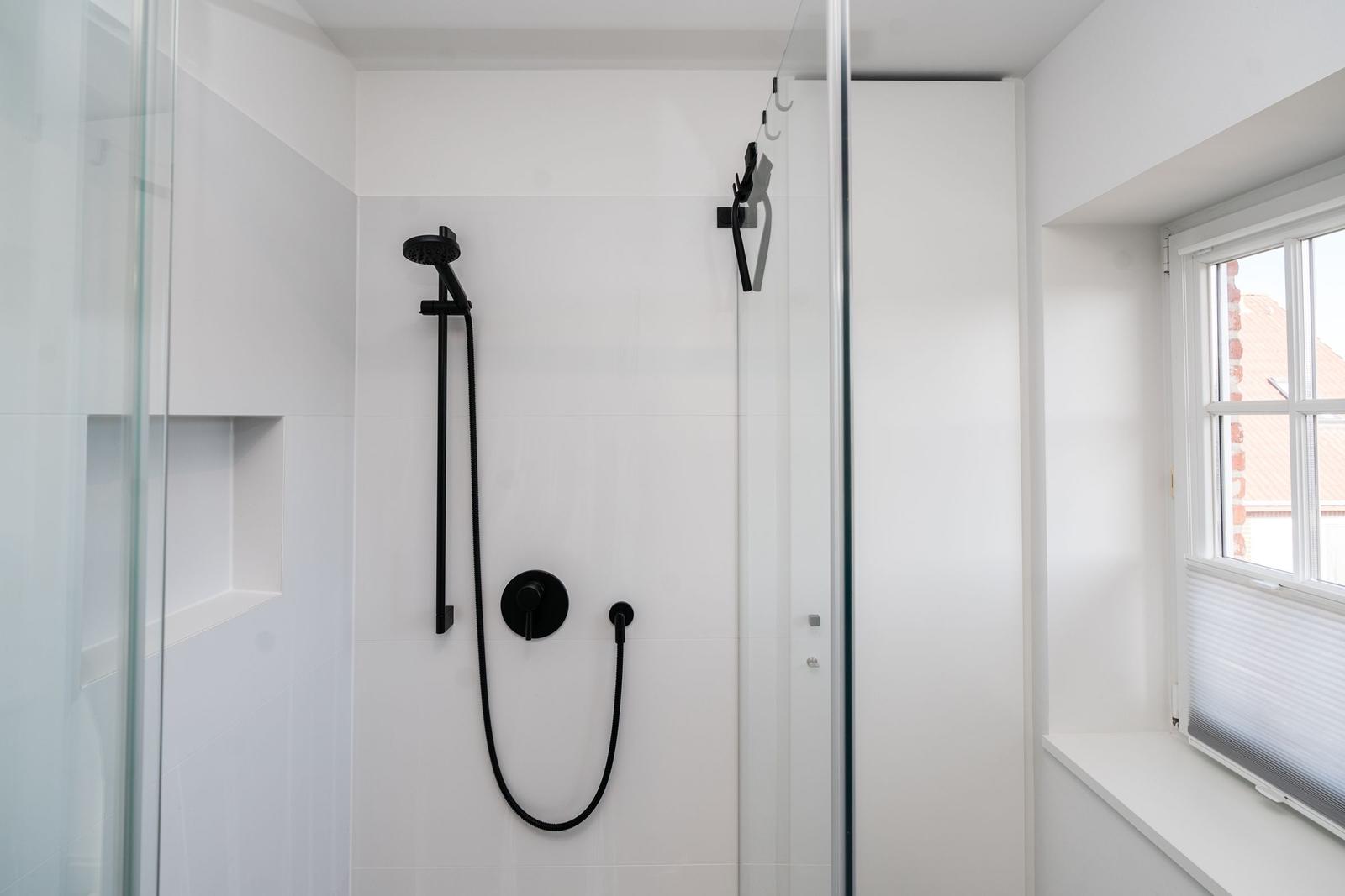 Dusche mit schwarzen Armaturen und Glaswand. Fenster mit Jalousie.