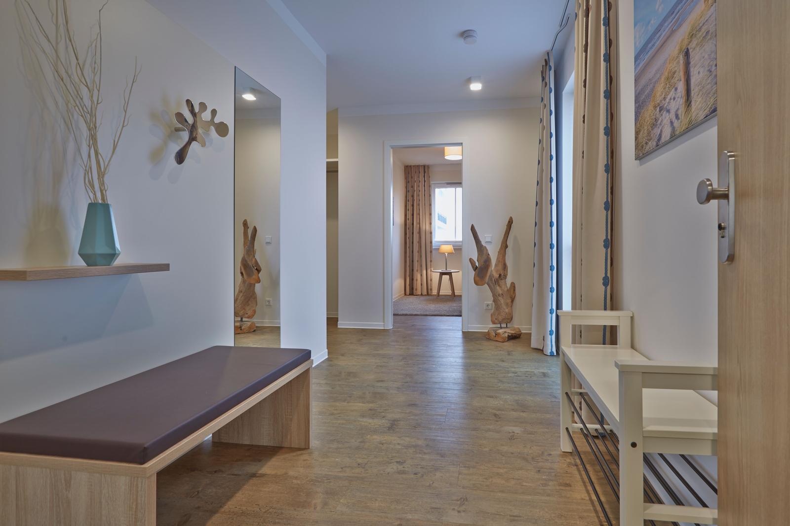 Flur mit Holzboden, Sitzbank und Wanddekoration. Durchgang zu Wohnraum mit Fenster.