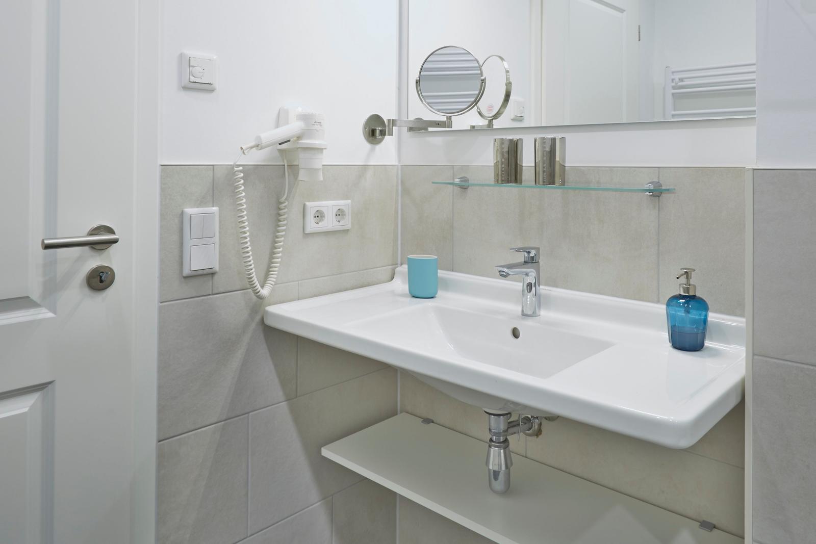 Badezimmer mit Waschbecken, Spiegel und Handtuchhalter.