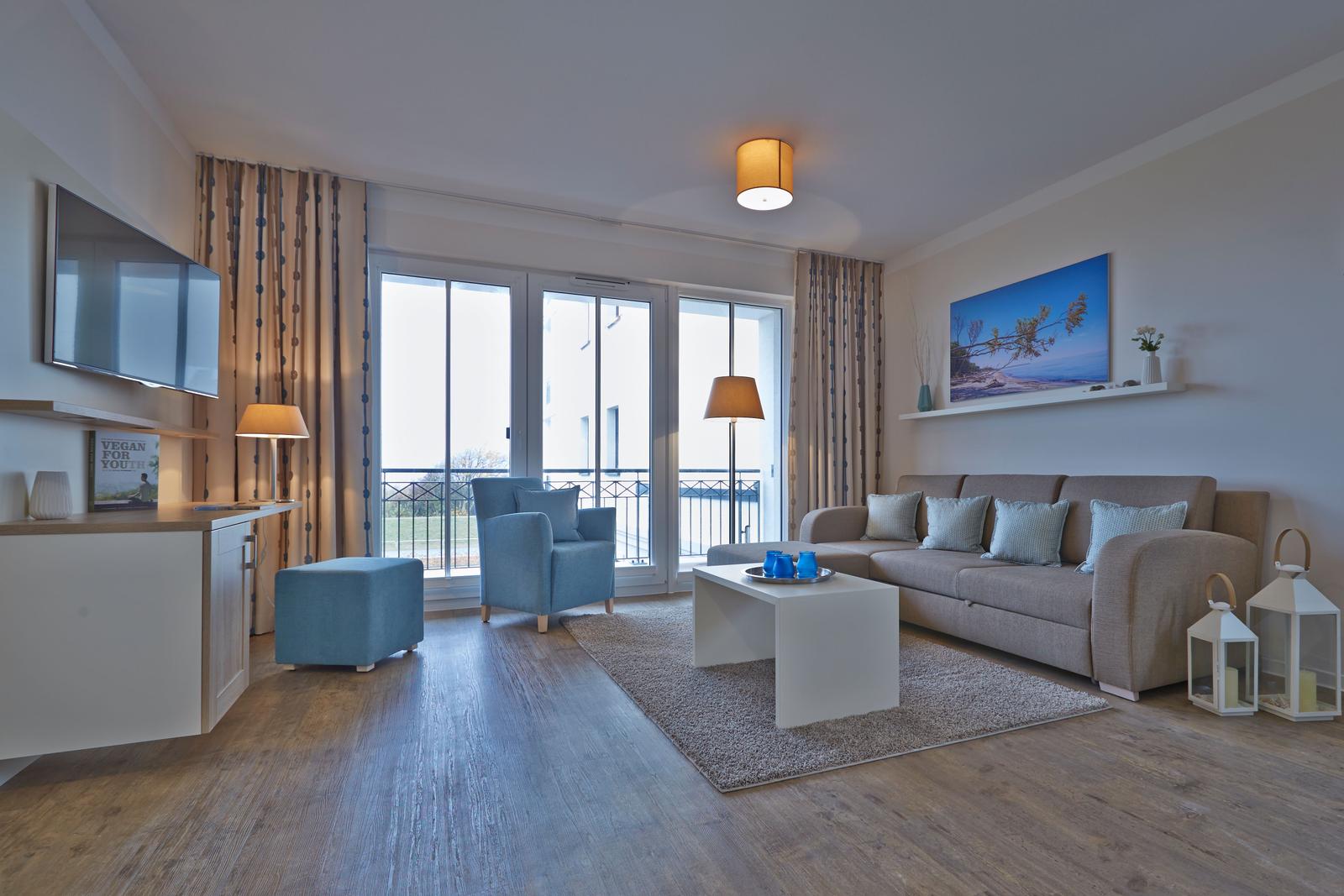 Wohnzimmer mit Sofa, Sessel und Balkonansicht.