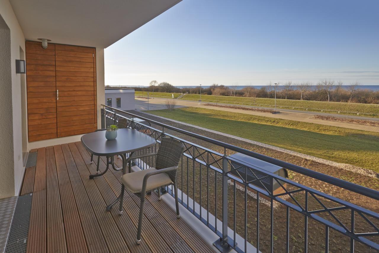 Terrasse mit Tisch und Stühlen, Blick auf Grünfläche und Wasser.