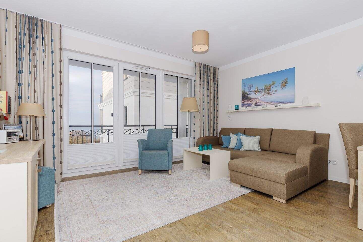 Wohnzimmer mit Sofa, Sessel und Balkonansicht.