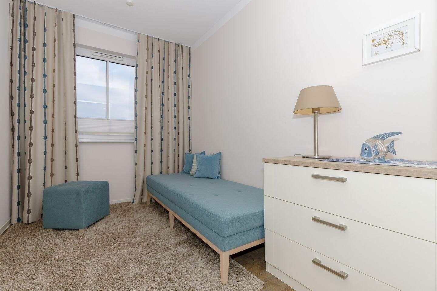 Schlafzimmer mit blauer Couch, Schrank und Fenster mit Vorhängen.