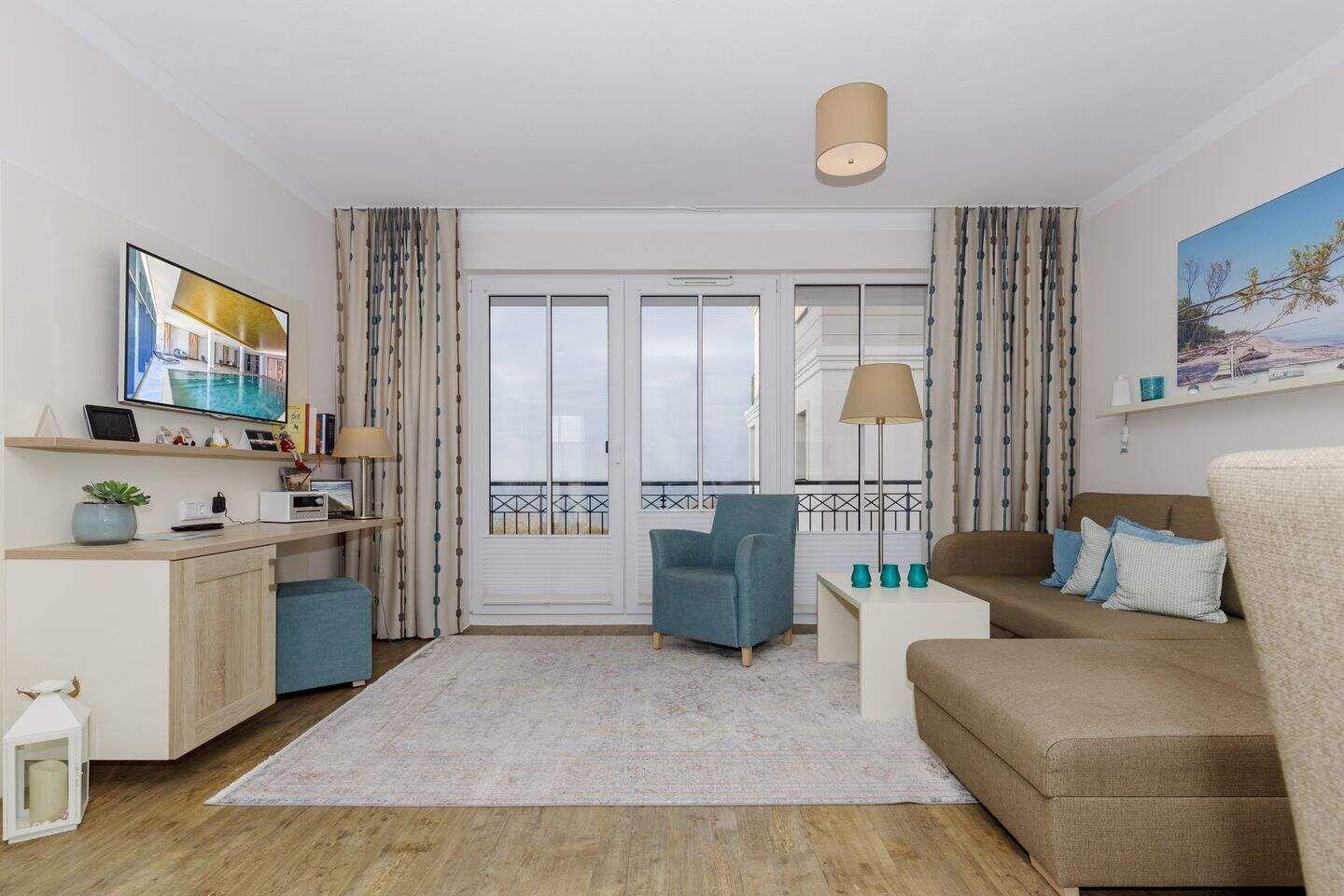 Wohnzimmer mit Sofa, Sessel, TV und Balkonzugang.