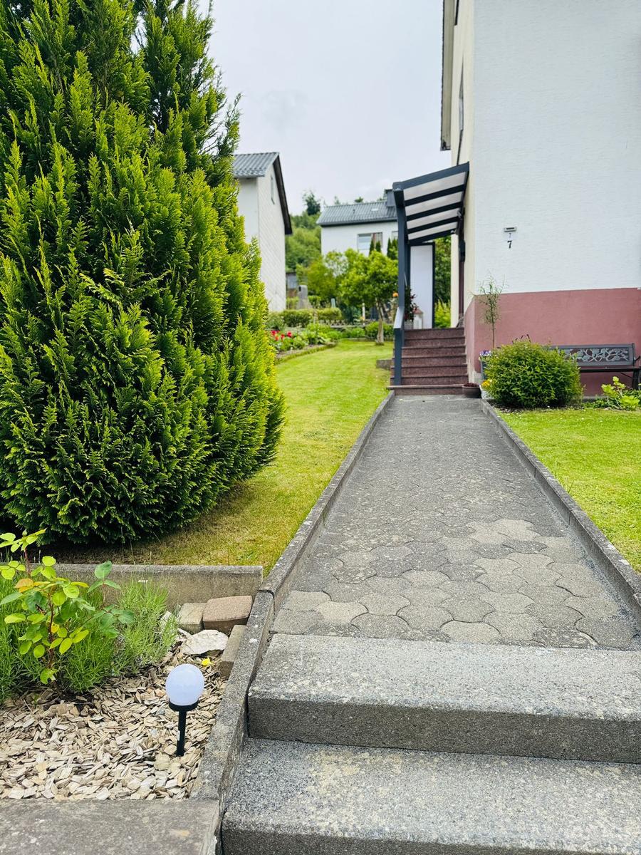 Gartenweg mit Stufen führt zur Haustür. Grünflächen und Sträucher umgeben den Eingang.