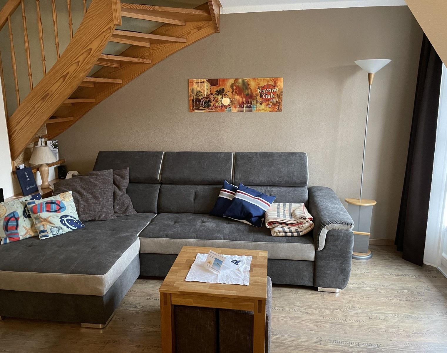 Wohnzimmer mit grauem Sofa, Holztisch und Holztreppe.