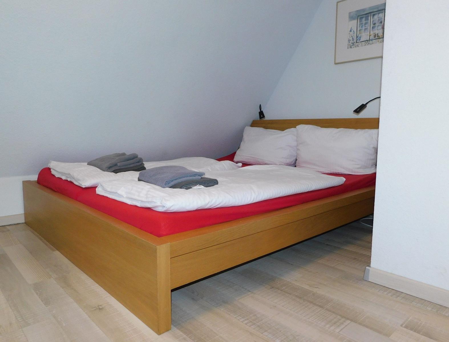 Ein Bett mit weißer Bettwäsche und rotem Matratzenbezug in einem Zimmer mit Holzboden.