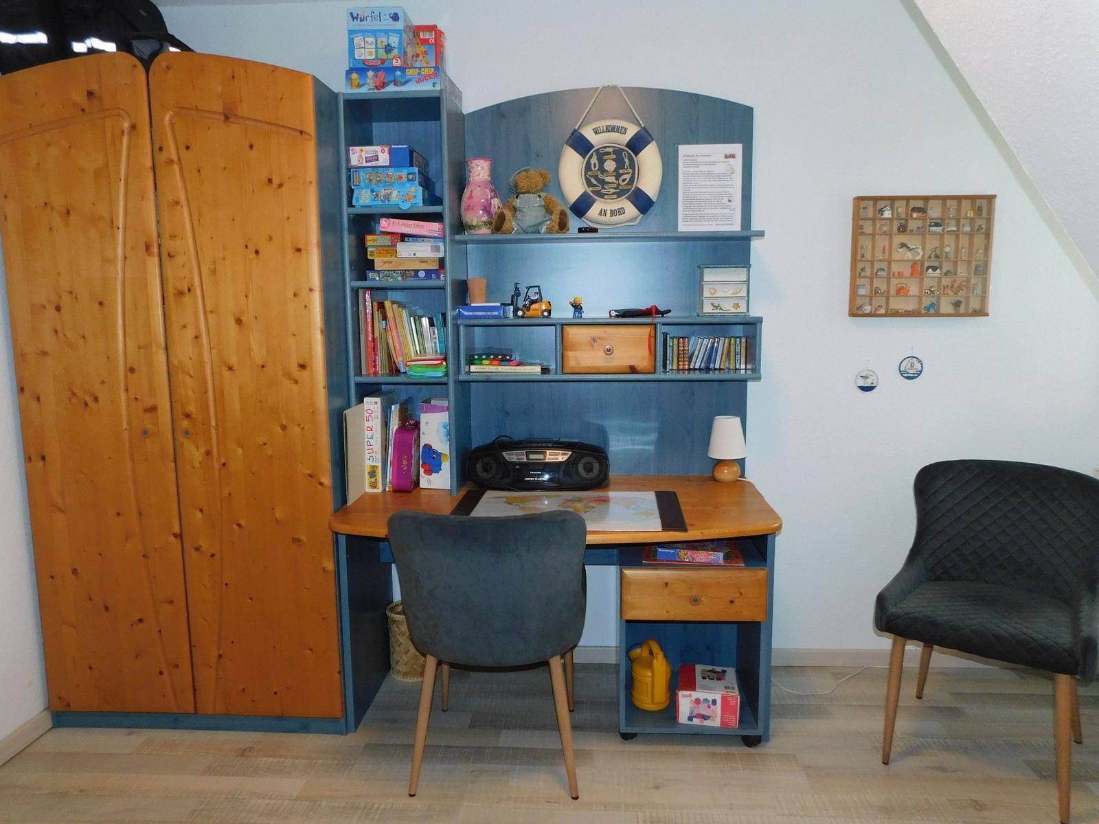 Schreibtisch mit Stuhl, Regal und Kleiderschrank in einem Kinderzimmer.