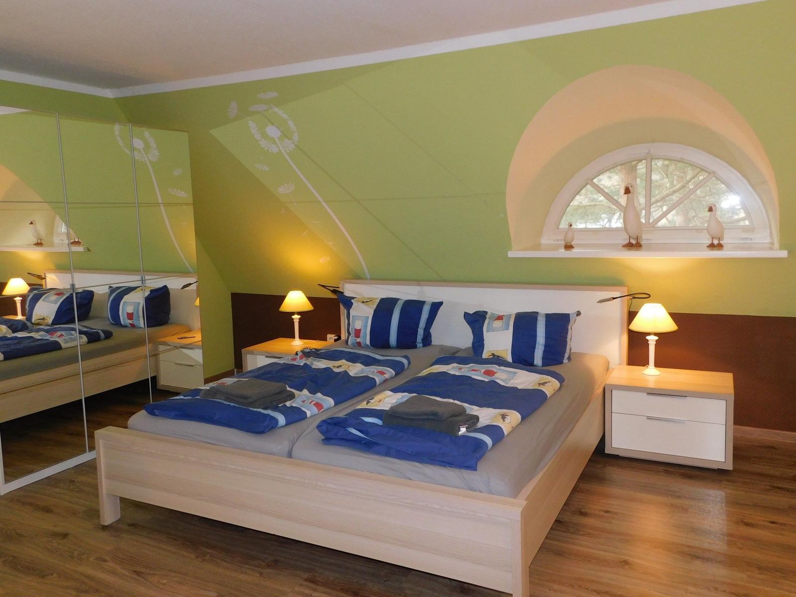 Doppelbett mit blauer Bettwäsche, Nachttische und Spiegelwand im Schlafzimmer.