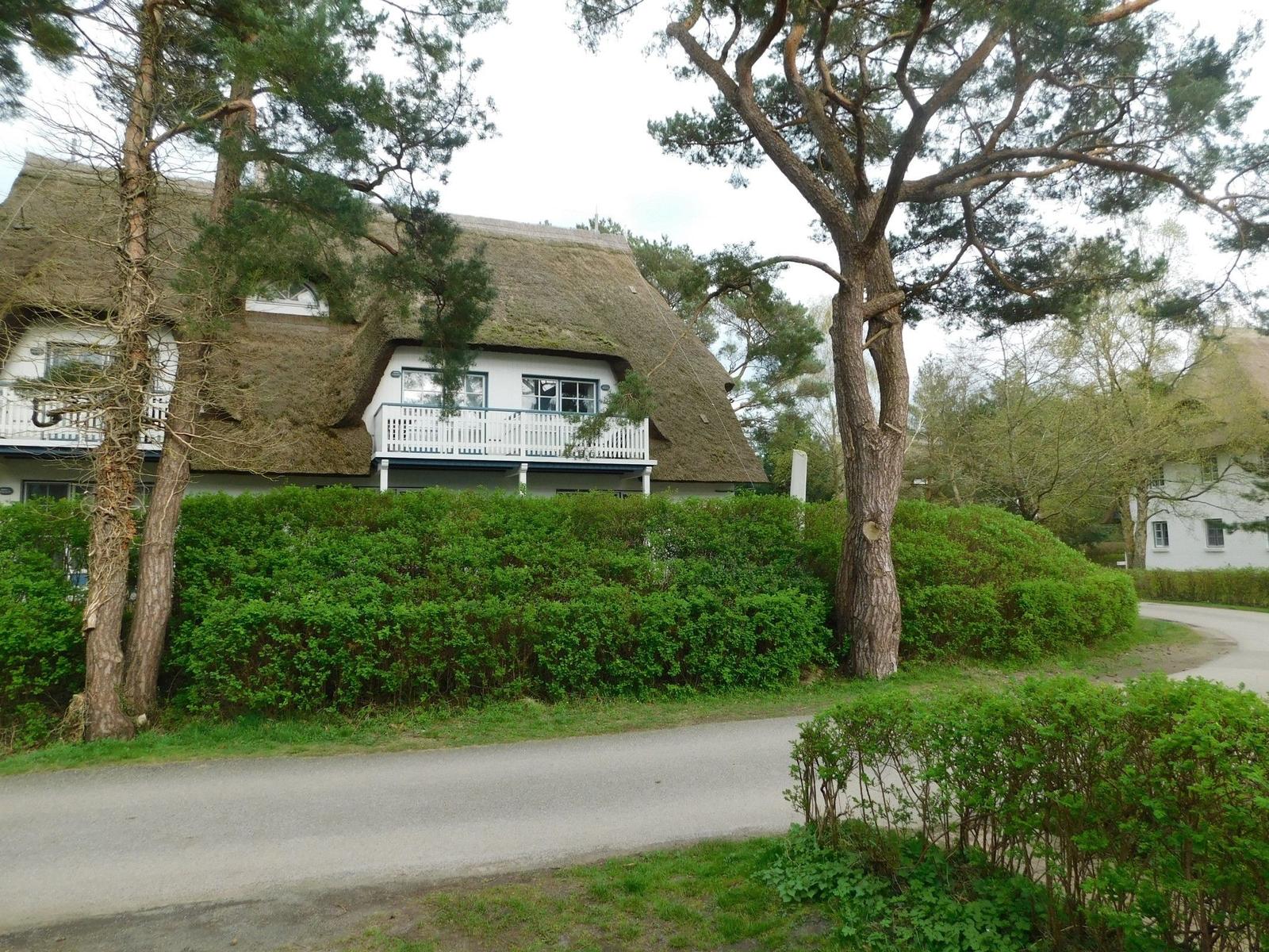 Haus mit Strohdach, weißer Veranda und grüner Hecke