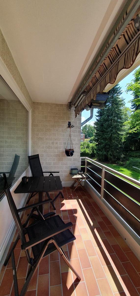 Balcony with table, chairs, and hanging plant overlooking greenery.