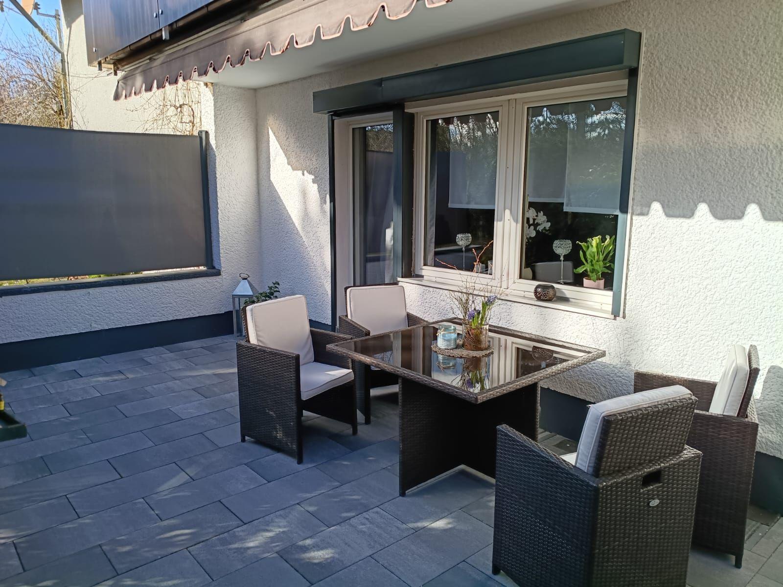 Terrasse mit Sitzgruppe, Tisch und Sonnenschutz. Fenster mit Pflanzen.