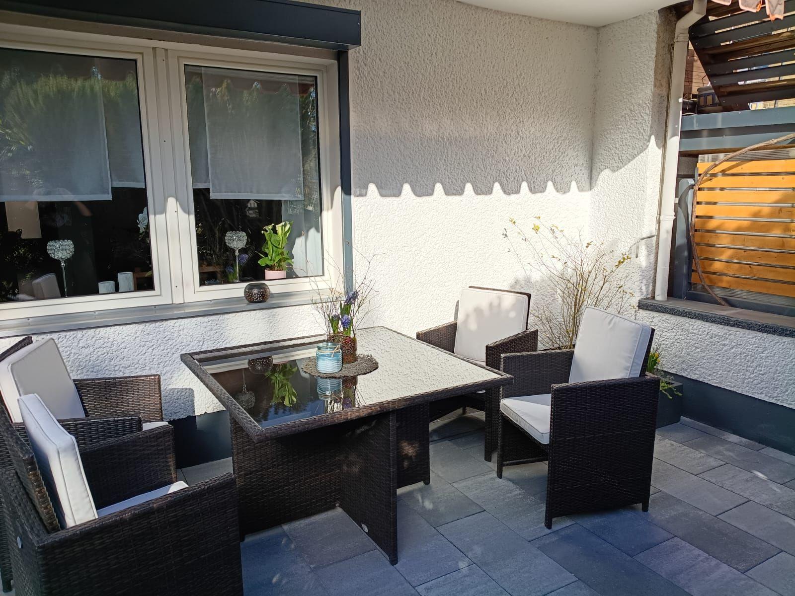 Terrasse mit Sitzgruppe, Tisch und Pflanzen. Wand und Boden sind sichtbar.