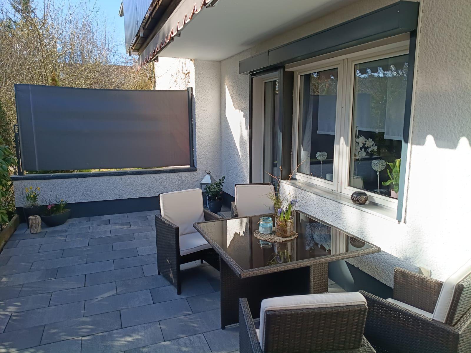 Terrasse mit Sitzgruppe, Sonnenschutz und Pflanzen. Glas-Tisch und Fenster zur Wohnung.