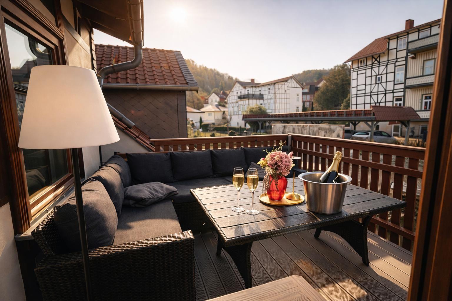 Terrasse mit Sitzgruppe, Tisch, Champagner und Blumen. Blick auf Fachwerkhäuser und Hügel.