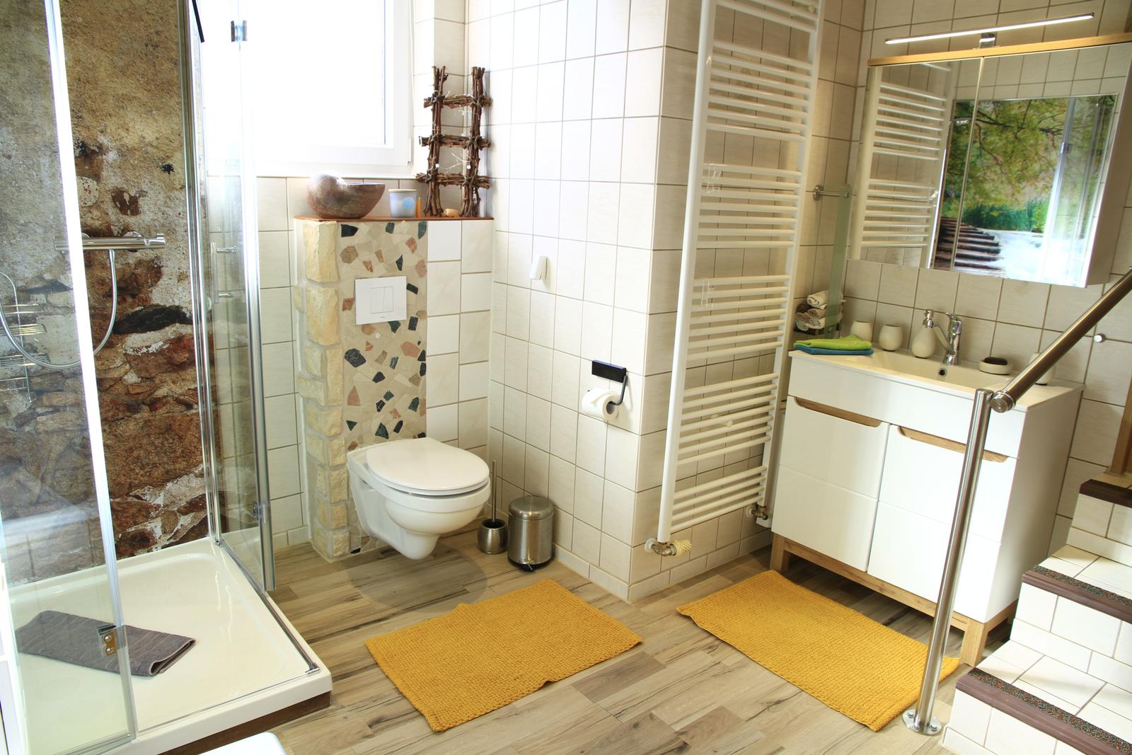 Bad mit Dusche, Toilette und Waschbecken. Holzdielenboden und gelbe Teppiche.