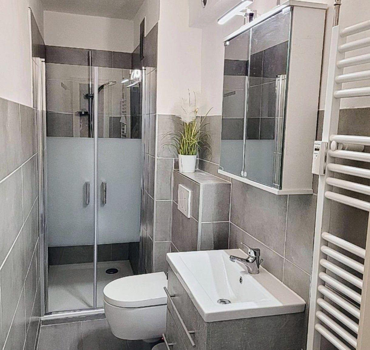 Badezimmer mit Dusche, Waschbecken und Toilette. Graue Fliesen und Spiegelschrank.