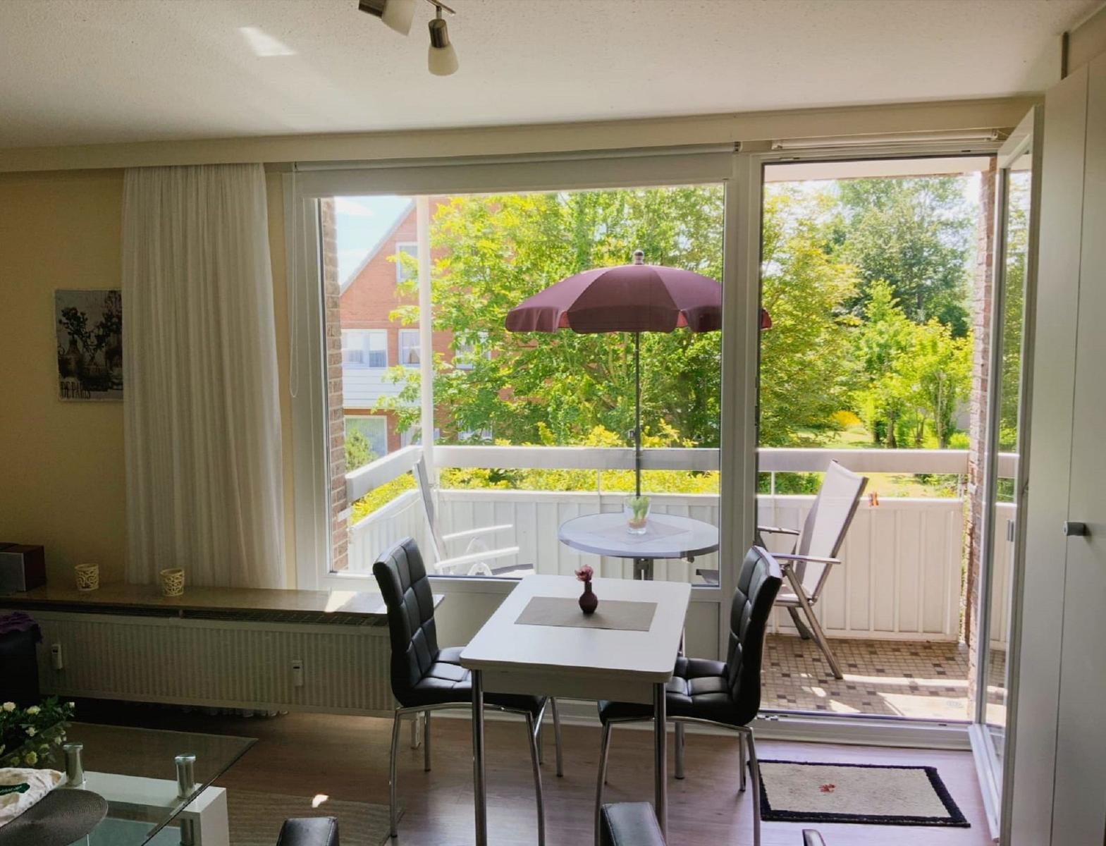 Essbereich mit Blick auf Balkon mit Tisch, Stühlen und Sonnenschirm.