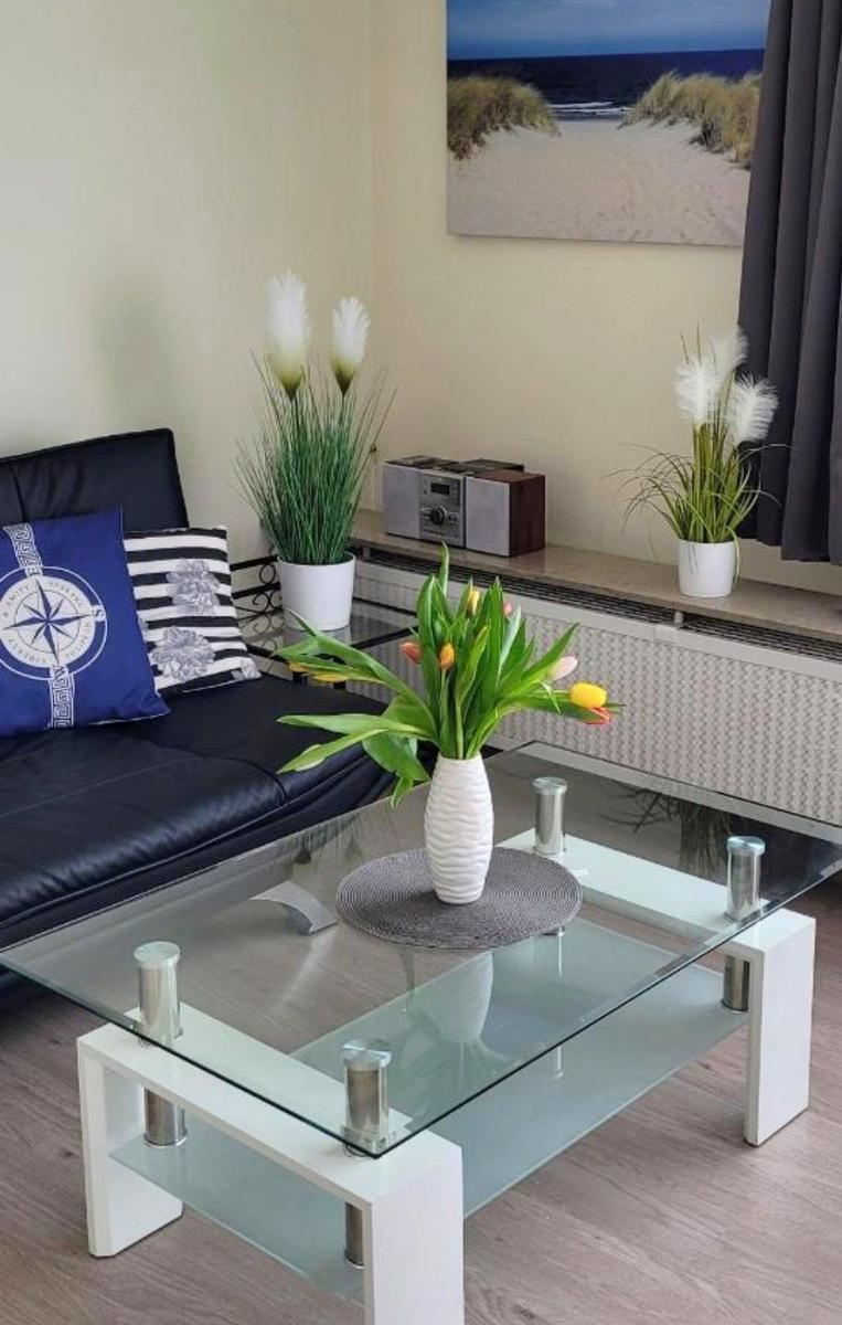 Schwarzes Sofa mit Kissen, Glas-Tisch und Blumen. Wandbild zeigt Strand.